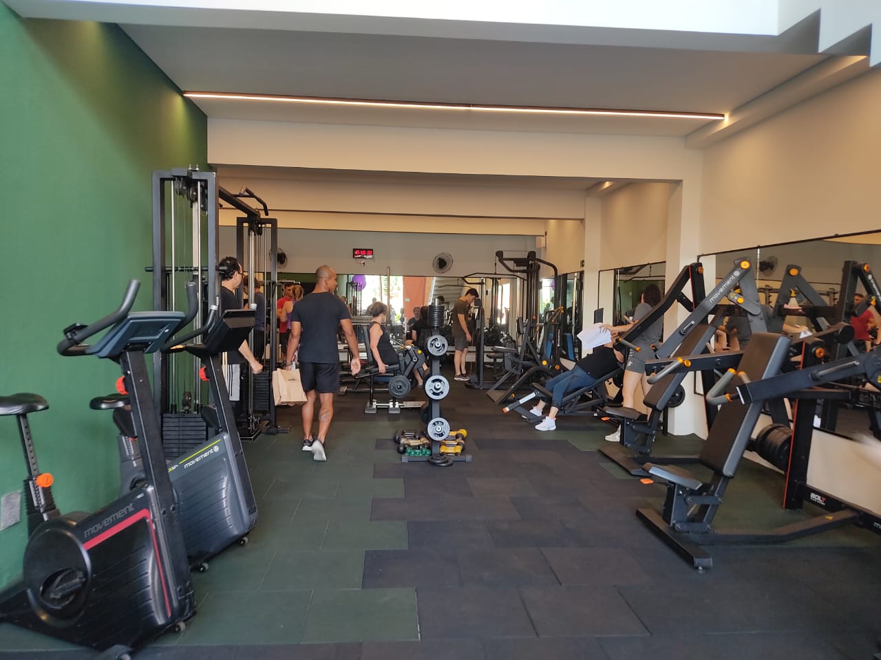 Sala da BIOFIT: aparelhos pretos, parede verde e alunos treinando